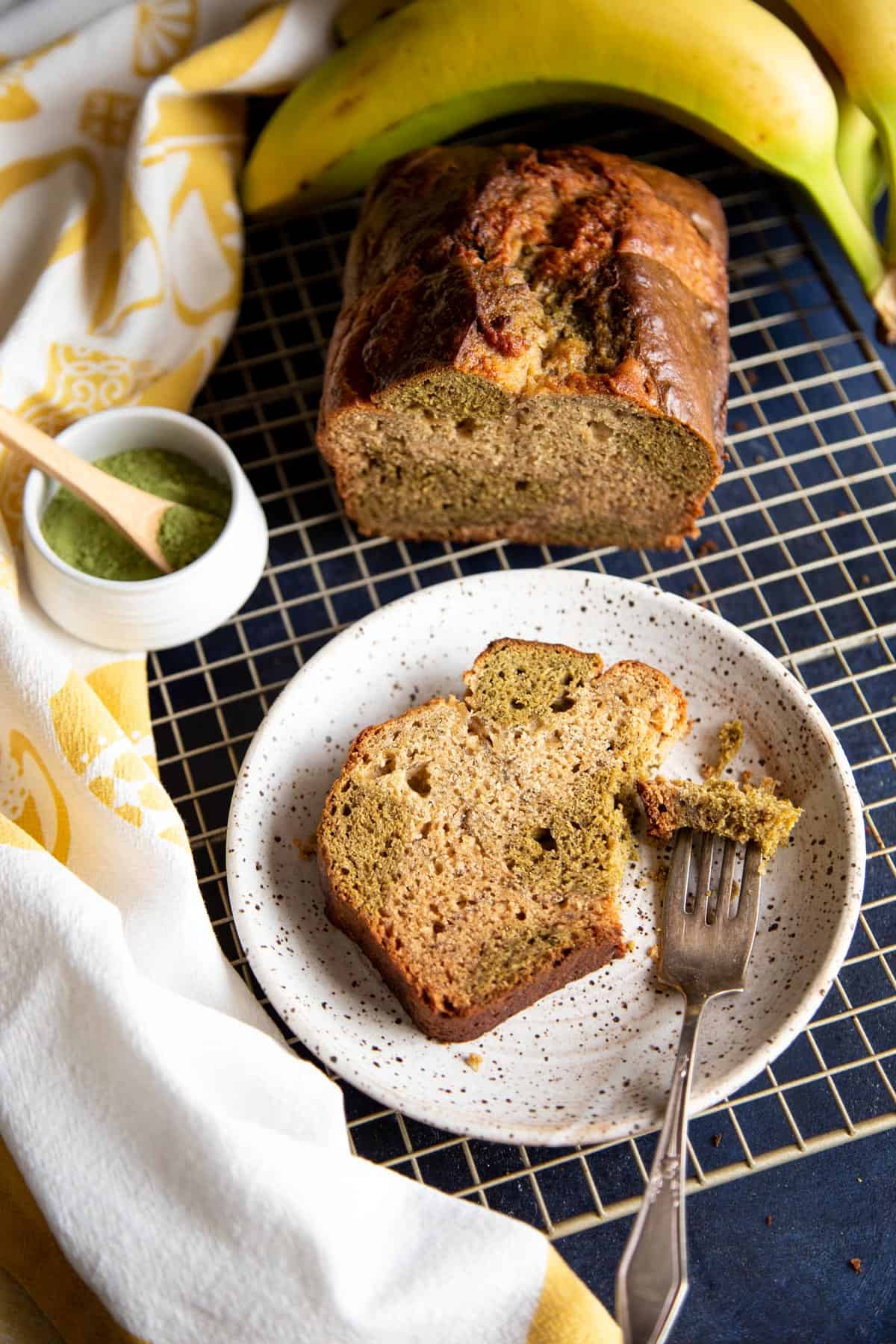 A slice of matcha banana bread on a plate next to half a loaf.