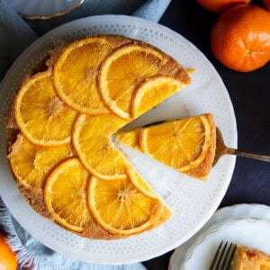 Orange upside down cake on a white cake stand with a slice on a cake server.