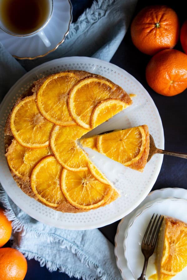 Orange upside down cake on a white cake stand with a slice on a cake server.