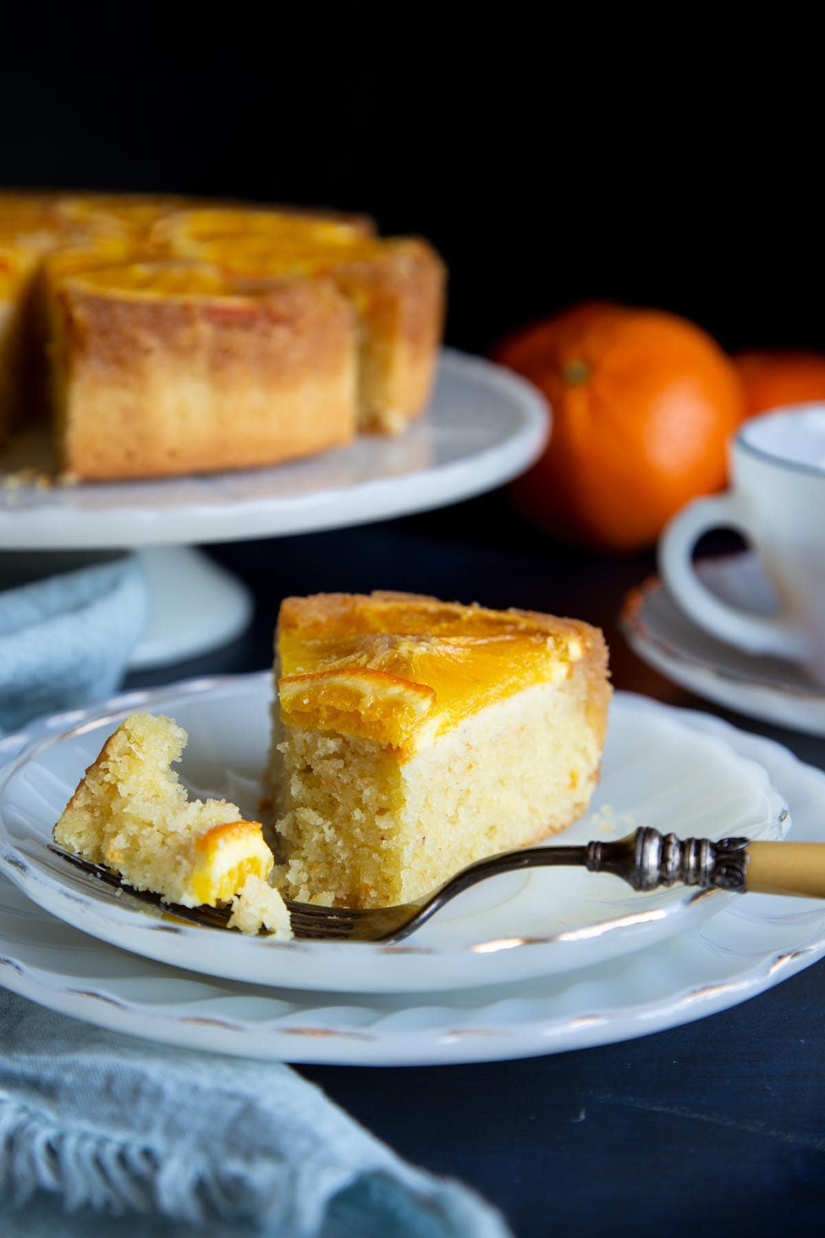 A slice of orange almond cake on a plate with a piece of cake on a fork.