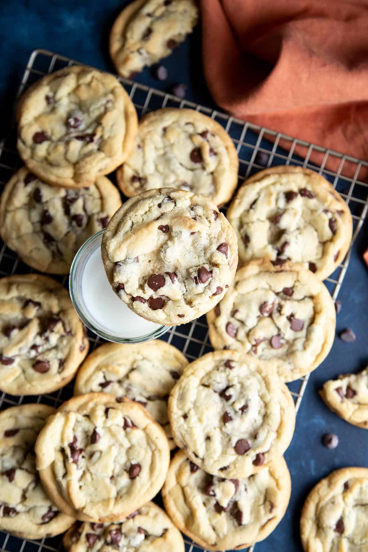 Chocolate chip cookies on a wire rack with a glass of milk.