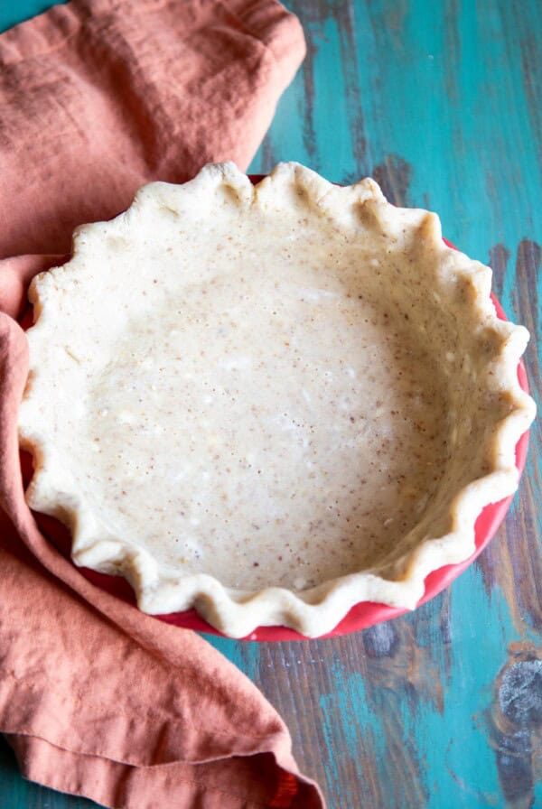An unbaked pecan pie crust next to an orange towel.