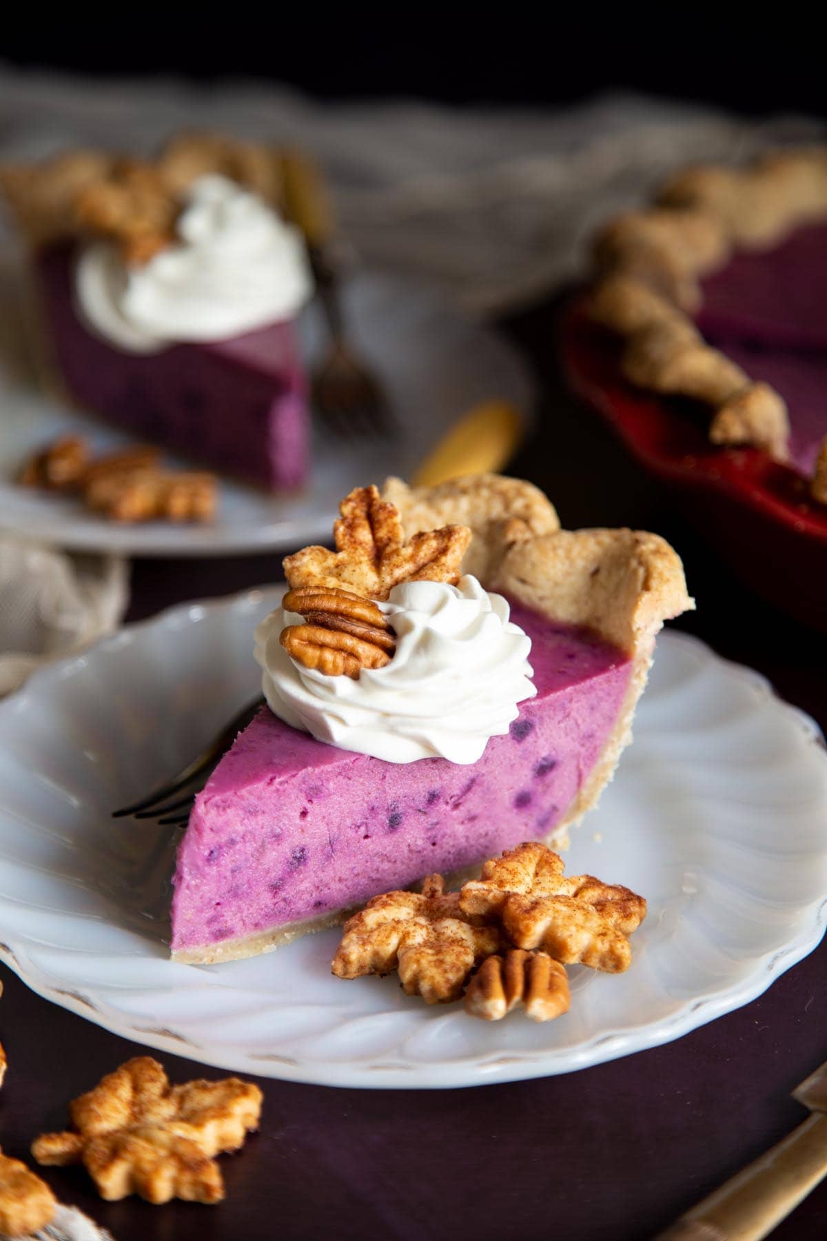 A slice of purple sweet potato pie on a plate with maple leaves cookies and pecans.