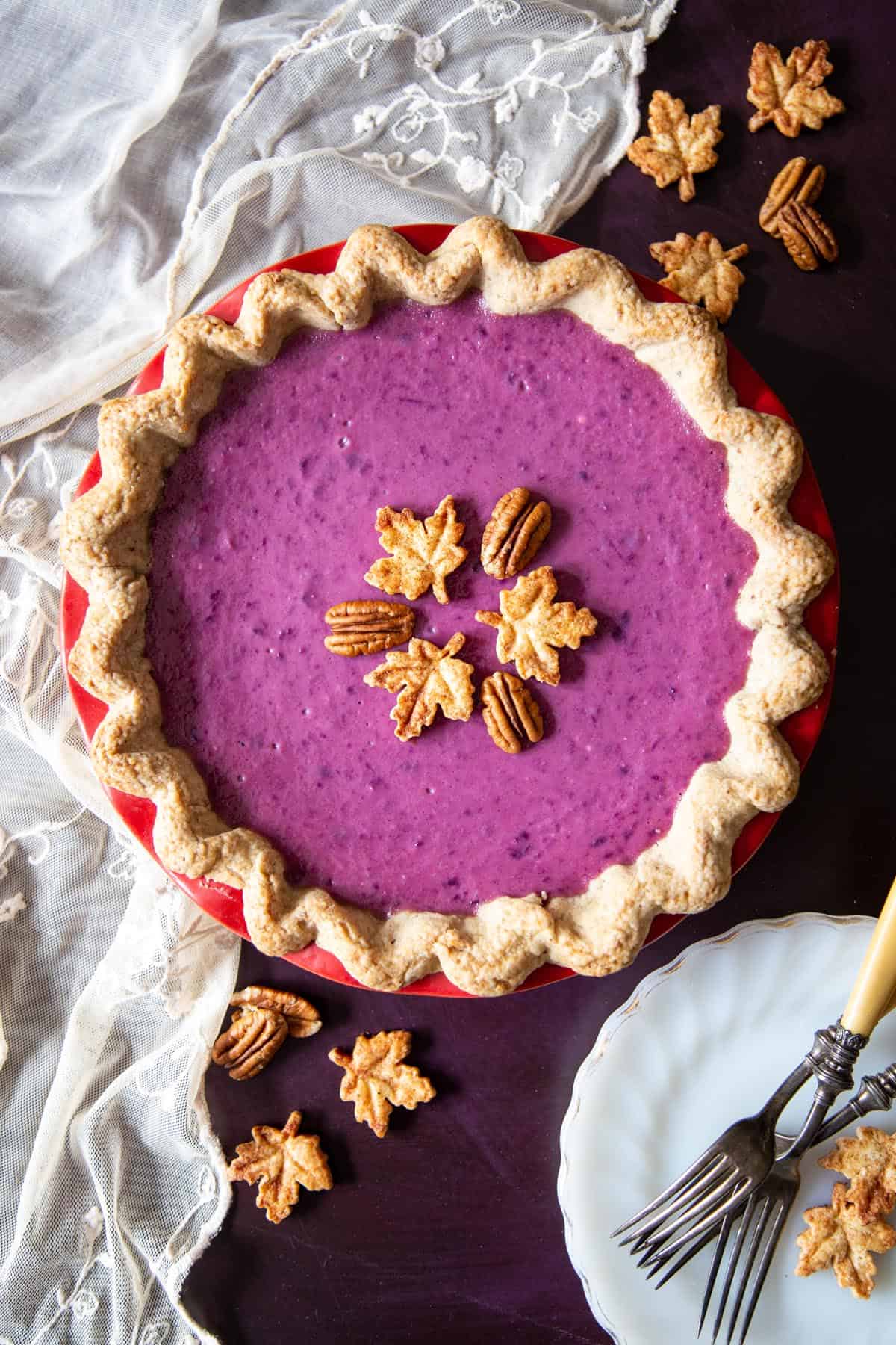 A purple sweet potato pie decorated with maple leaves cookies and pecans.