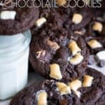 A pile of chocolate marshmallow cookies next to a glass of milk.