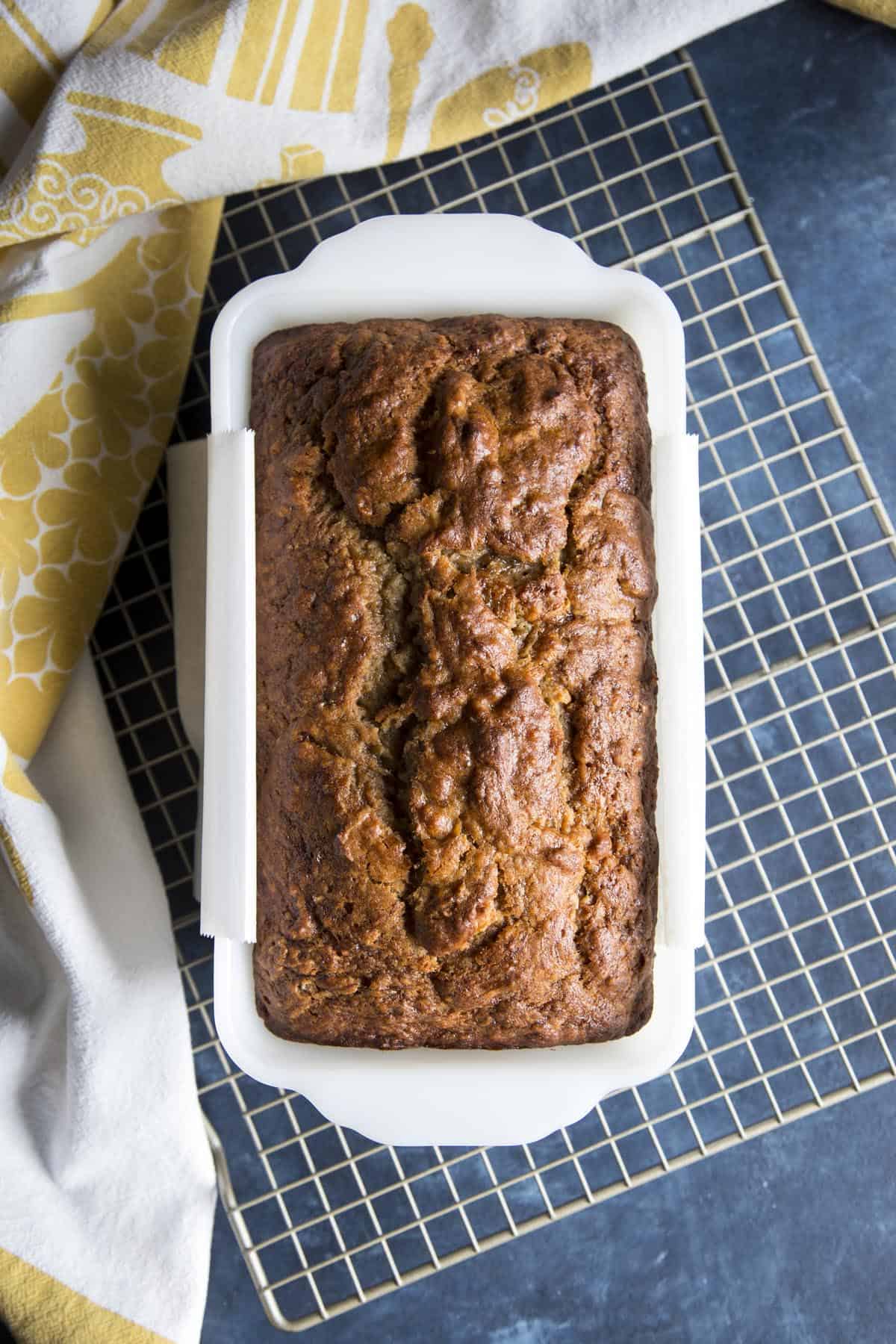 Baked banana bread in a loaf pan on a cooling rack.