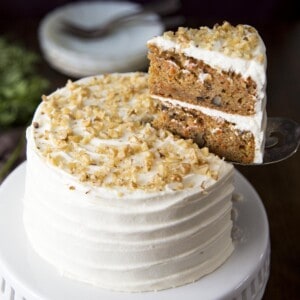 A mini carrot cake on a white cake stand with a slice being cut.