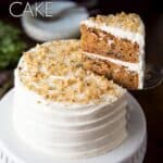 A mini carrot cake on a white cake stand with a slice being cut.