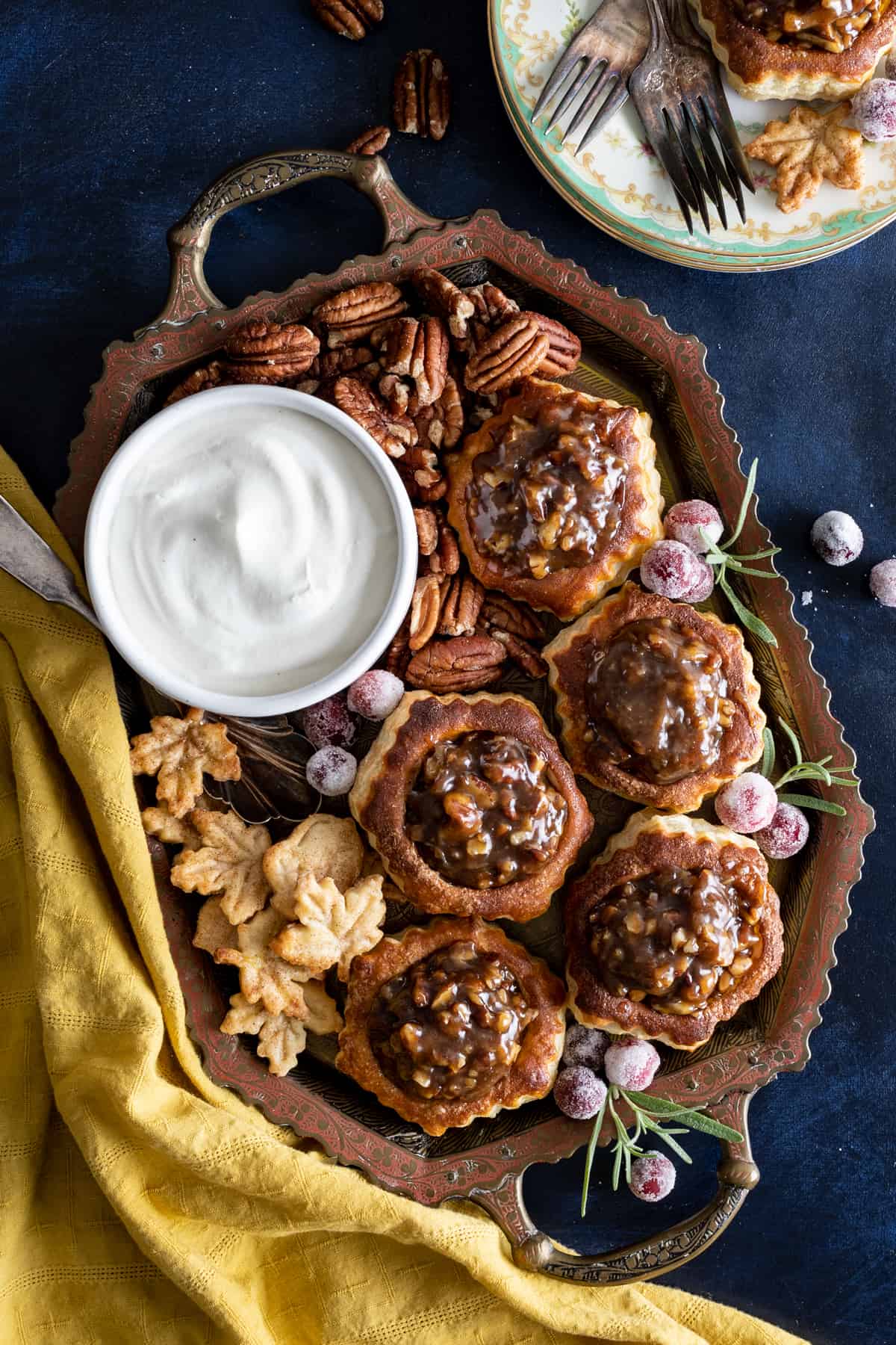 A bowl of chantilly cream on a tray with mini pecan tarts.