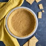 A graham cracker crust next to a yellow tea towel and crackers around it.