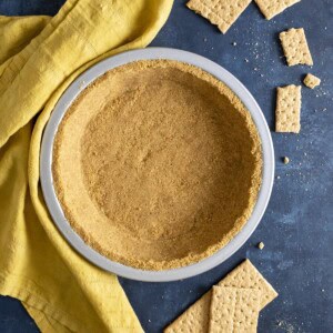 A graham cracker crust next to a yellow tea towel and crackers around it.