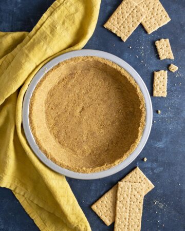 A graham cracker crust next to a yellow tea towel and crackers around it.