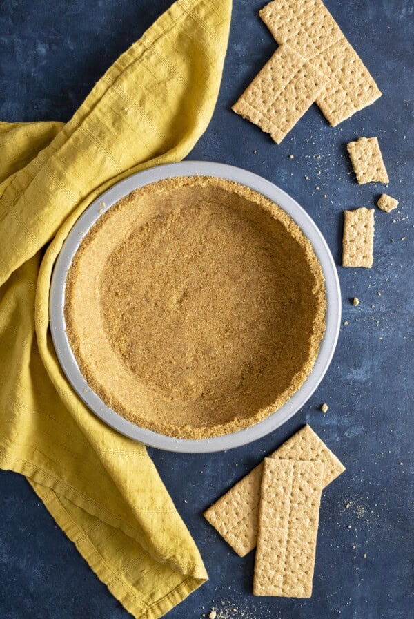 A graham cracker crust next to a yellow tea towel and crackers around it.