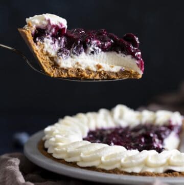 A slice of blueberry cream cheese pie is lifted up with a pie server.