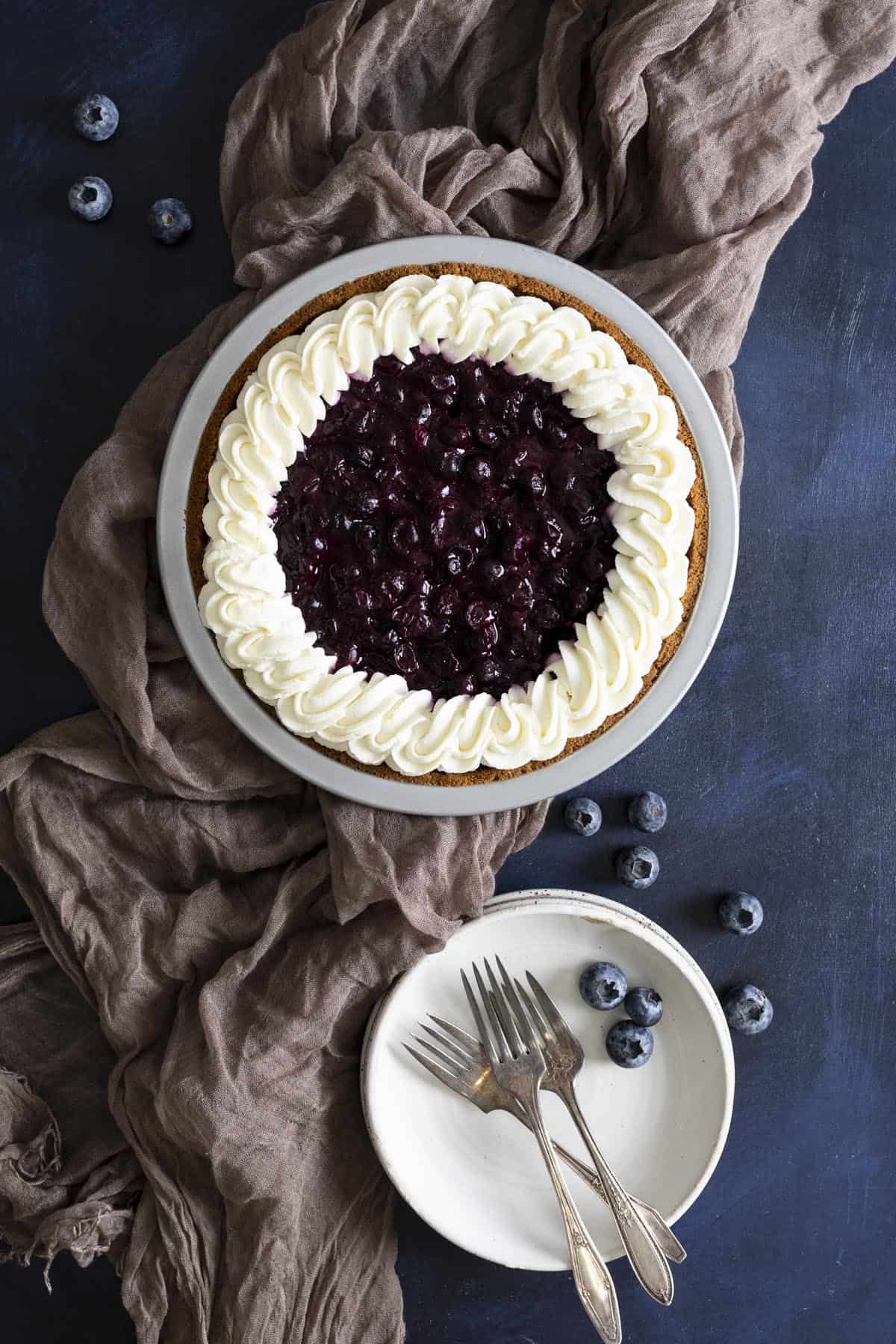 A no bake blueberry pie with Graham cracker crust next to a stack of white plates.