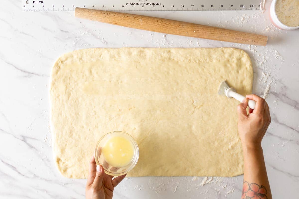 Brushing melted butter on the dough surface.