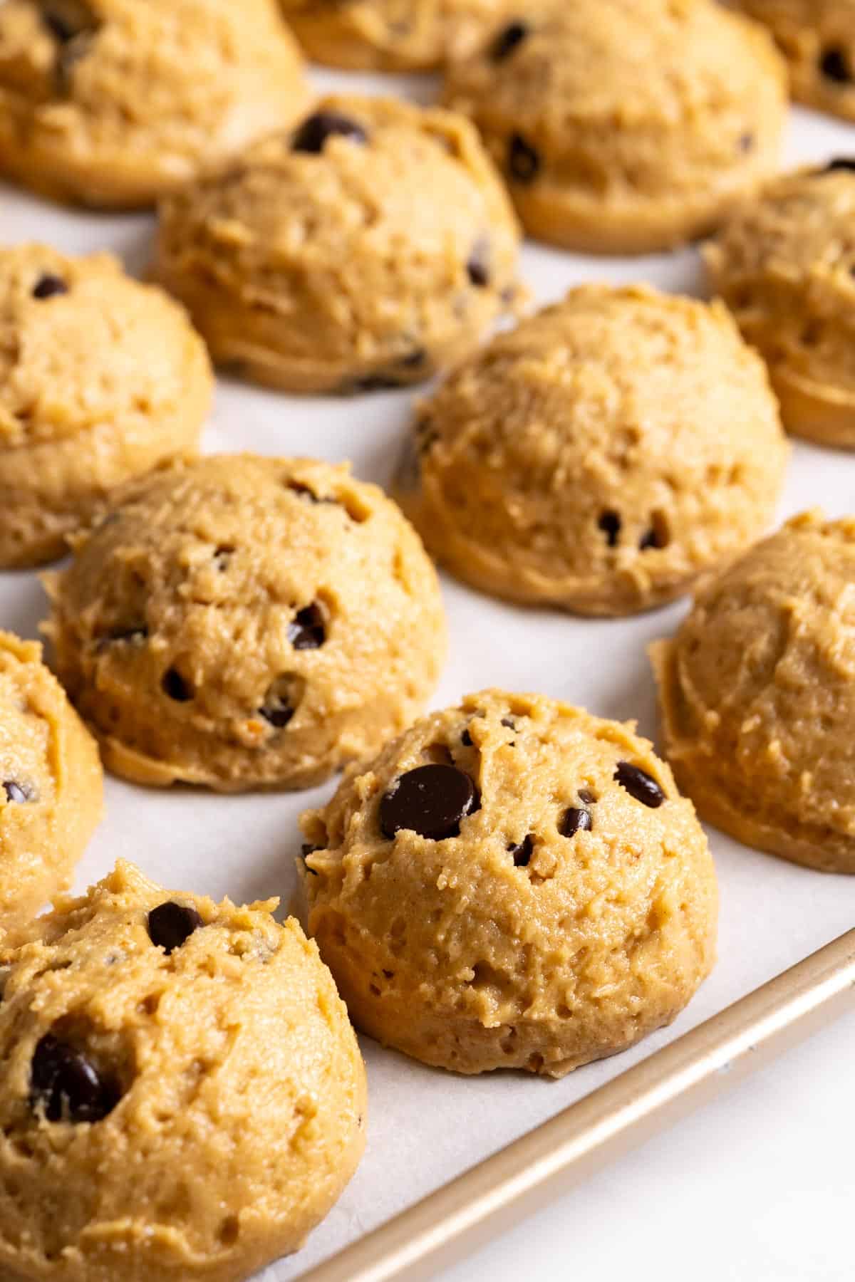 Toffee chocolate chip cookies dough divided up and placed on a lined baking sheet.