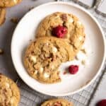 Two white chocolate raspberry cookies on a plate, one has a bit taken out of it.