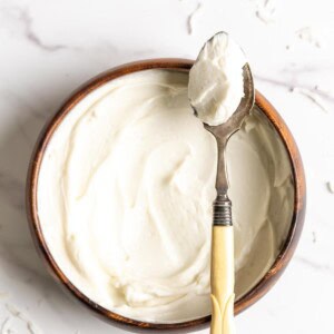 Coconut frosting in a wooden bowl with a spoon of frosting resting on top.