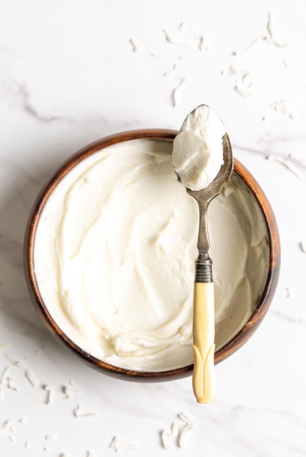 Coconut frosting in a wooden bowl with a spoon of frosting resting on top.