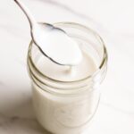 Coconut sauce is dripping down a spoon into a glass jar.