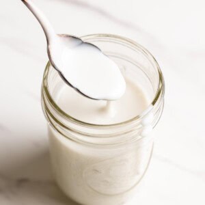 Coconut sauce is dripping down a spoon into a glass jar.