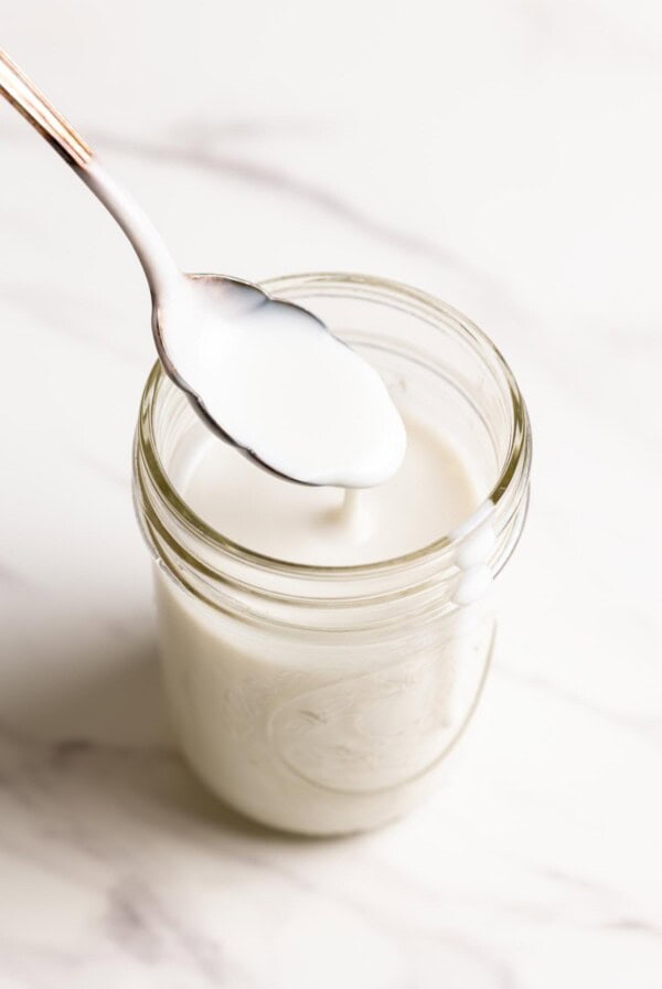 Coconut sauce is dripping down a spoon into a glass jar.