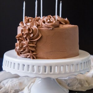 A small cake decorated with chocolate swiss meringue buttercream with some candles on it.