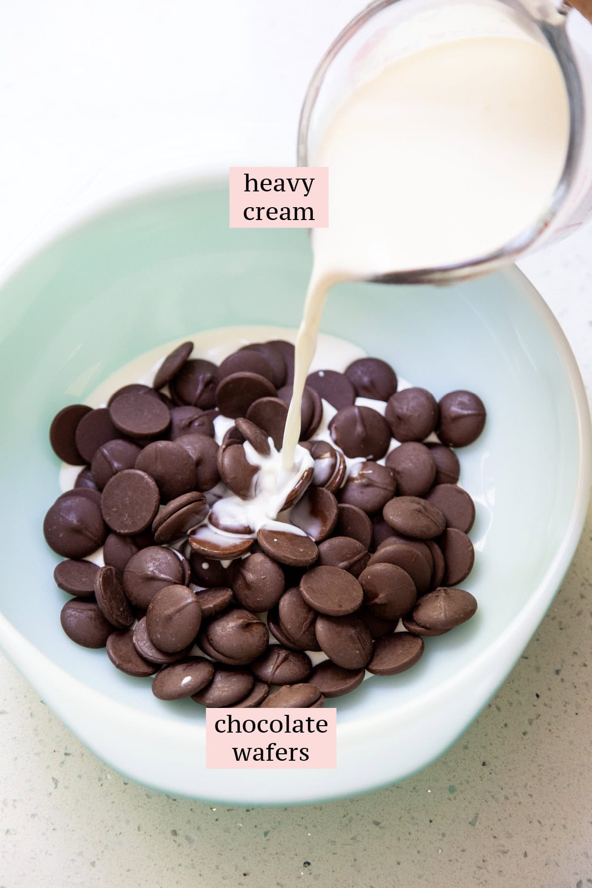 Heavy cream in a measuring cup is pouring into a bowl of chocolate.