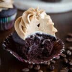 A mocha cupcake, half-eaten, next to some coffee beans.