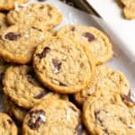 Coconut chocolate chip cookies piled on top of each other on a small baking sheet.