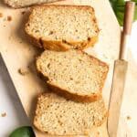 Three slices of banana coconut bread on a wooden cutting board next to a knife.