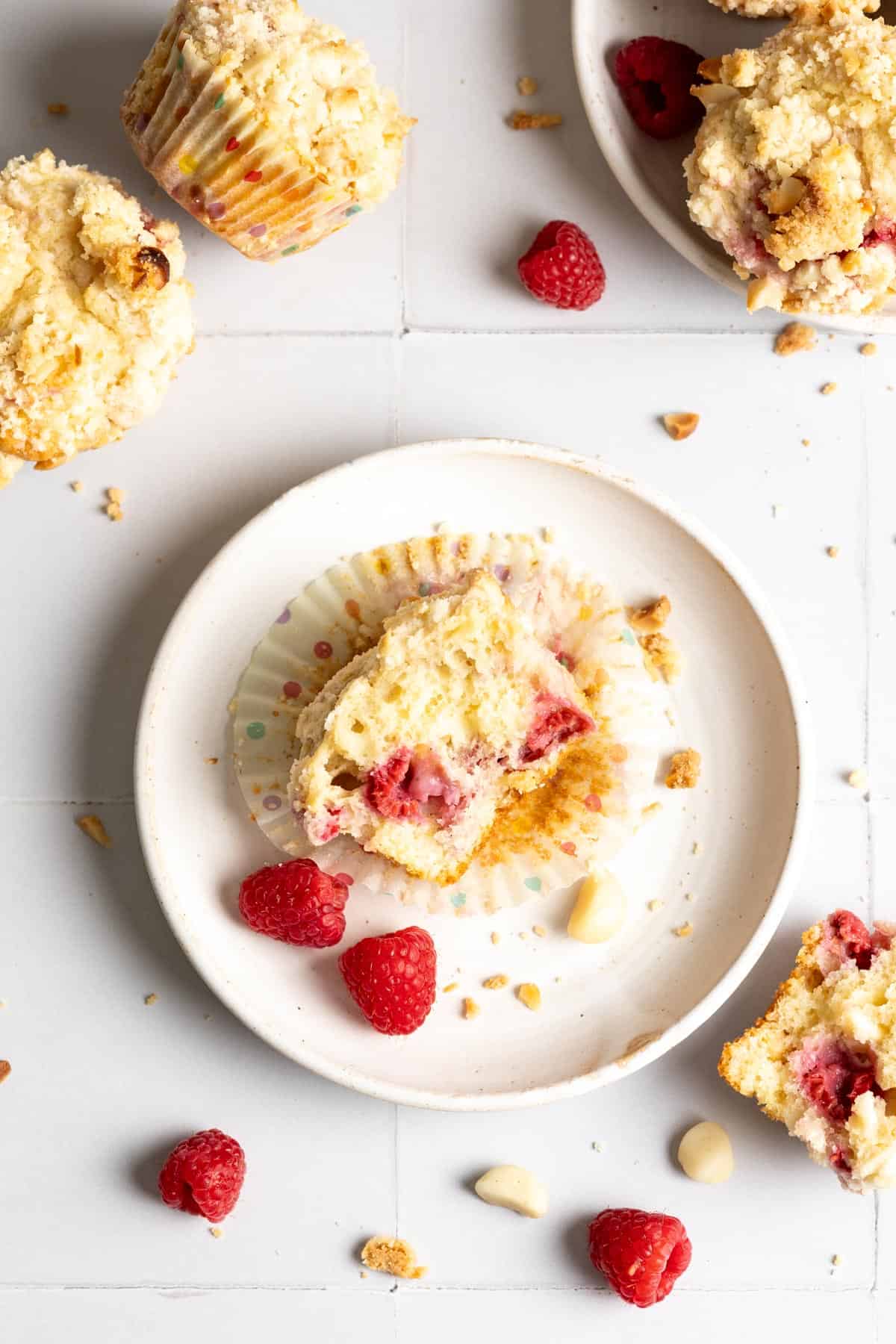 A raspberry and white chocolate muffin broke in half on white plate.