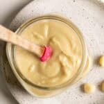 Top down view of a jar of macadamia nut butter with a pink spatula.