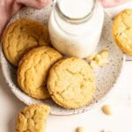 Three macadamia nut cookies on a plate with a small bottle of milk.