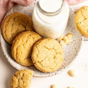 Three macadamia nut cookies on a plate with a small bottle of milk.