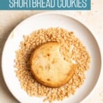 A toffee shortbread cookie sitting in a plate with toffee bits with a bite taken out of it.