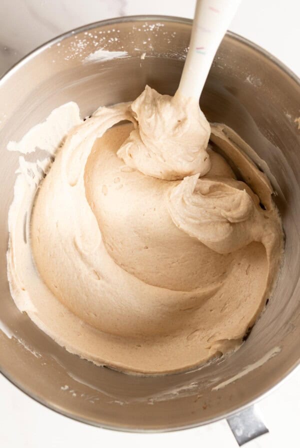 Creamy cinnamon cream cheese frosting in a stand mixer bowl with a spatula.