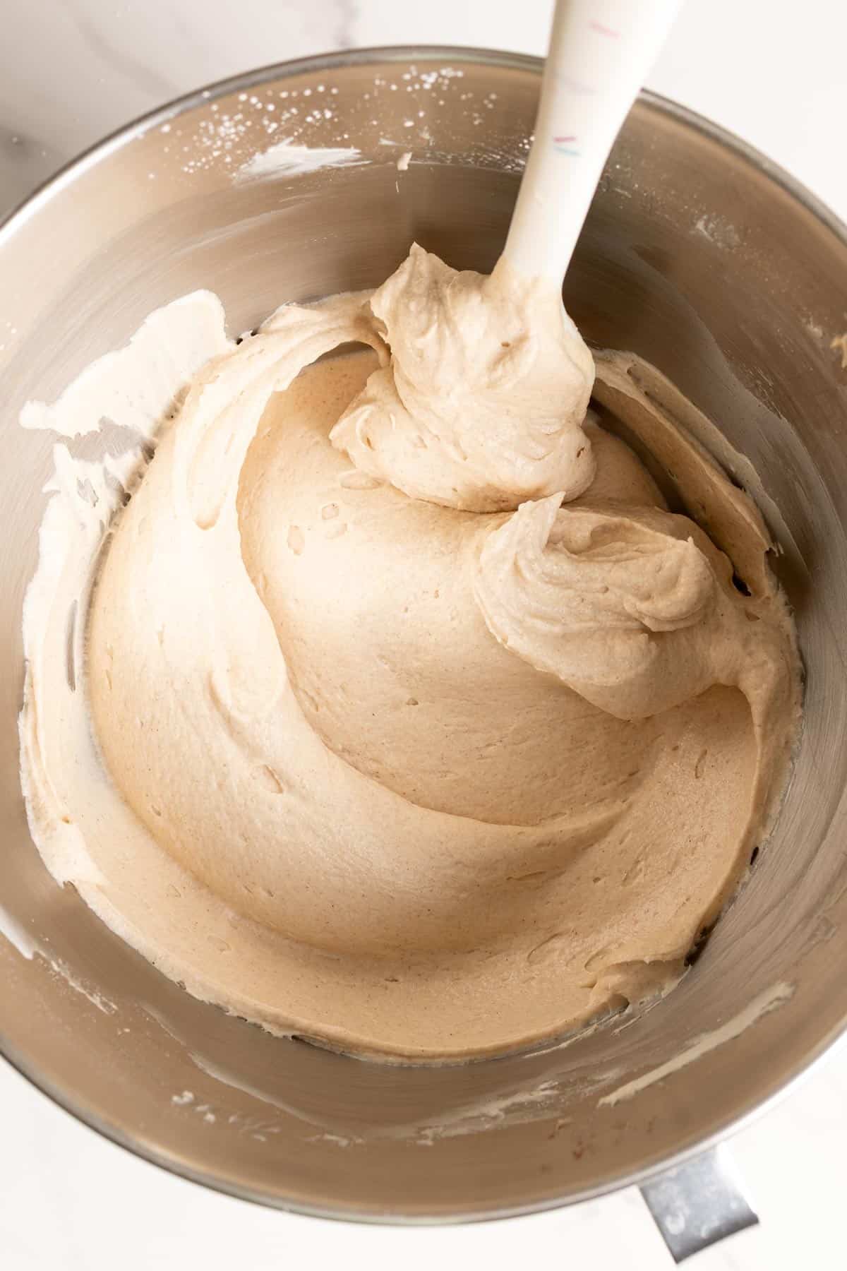 Creamy cinnamon cream cheese frosting in a stand mixer bowl with a spatula.