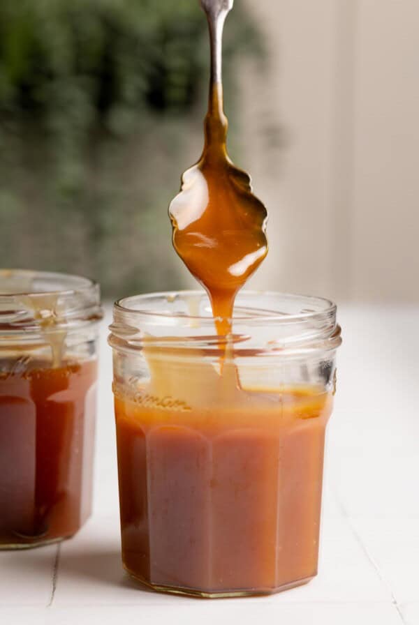 A spoonful of coconut caramel falling straight down into a glass jar.