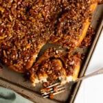Pecan sticky buns on a baking sheet, one bun is half eaten.
