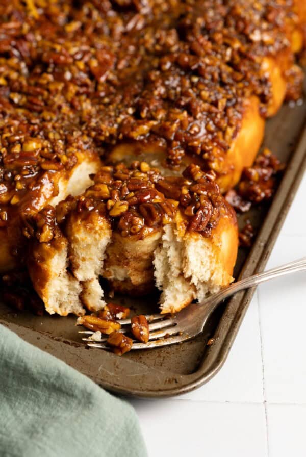A half eaten pecan sticky bun on a baking sheet with a whole batch of pecan sticky buns.