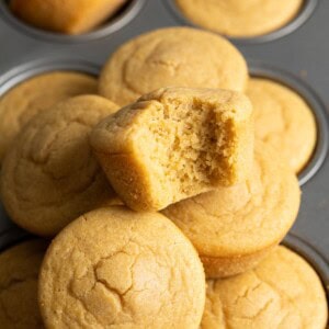 A half eaten mochi cornbread on top of a pile of mochi cornbread muffins.