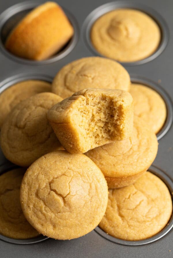 A half eaten mochi cornbread on top of a pile of mochi cornbread muffins.