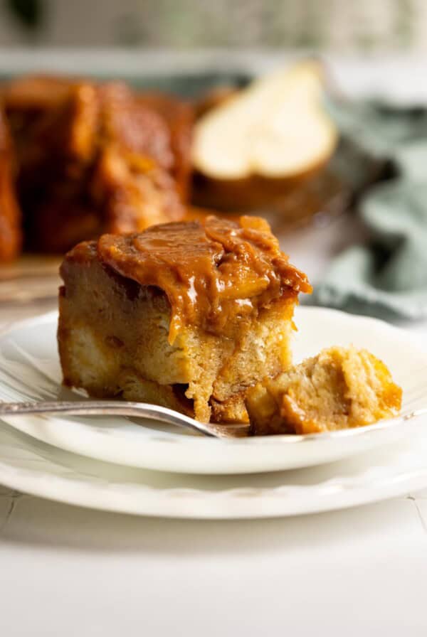 A slice of pear caramel bread pudding on a white plate with a bite on a fork.