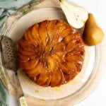 Bread pudding topped with sliced pear and miso caramel sauce on a glass serving plate.