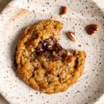 A single pecan oatmeal cookie on a plate with a bite taken out of it.