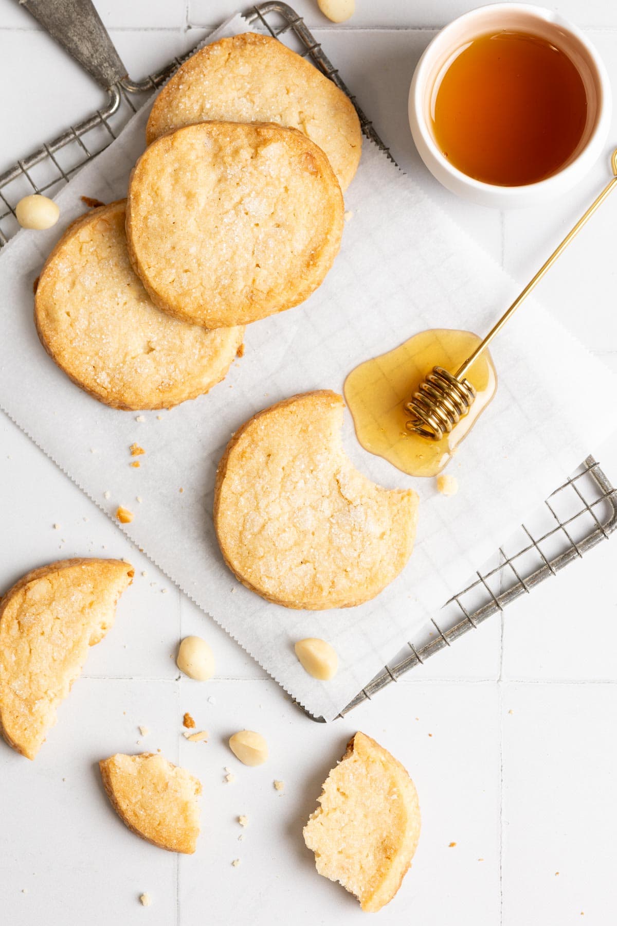 A few macadamia shortbread cookies on parchment next to a gold honey dipper.