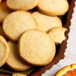 Close up of orange shortbread cookies on a tray with orange slices.