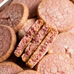 Three halved raspberry shortbread cookies nestled in a tray of cookies.